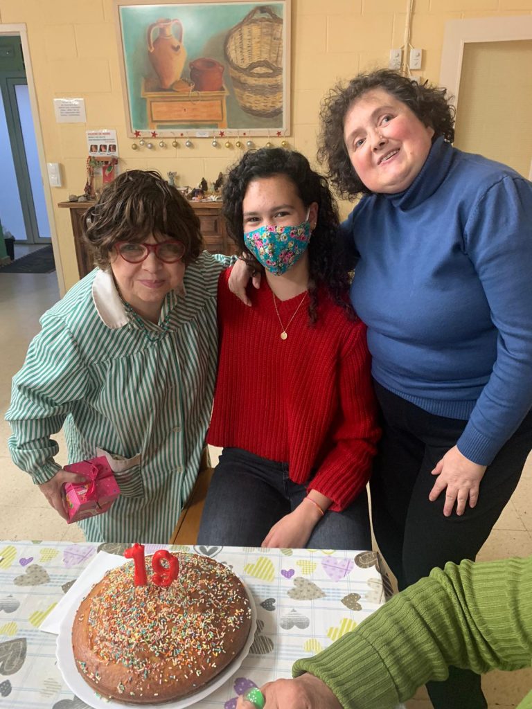 Trois personnes sont accolées. Aux extrémités des personnes plus âgées et au centre, une jeune fille. Elle célèbre ses 19 ans. Un gâteau avec un bougie est posé sur la table devant elle. Tous sourient à la caméra.